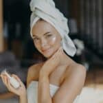Beautiful young European woman applies face cream, hydrates skin, wears minimal makeup