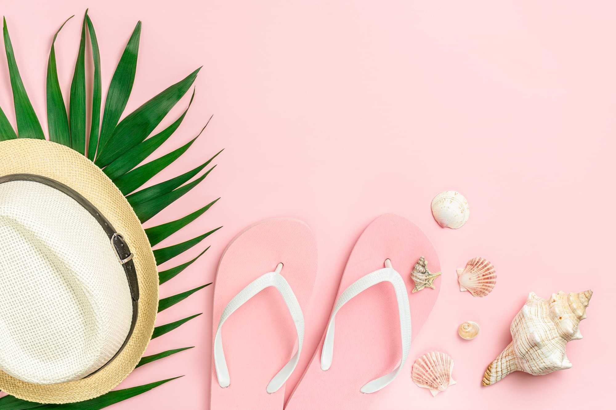 Pink background with flip flops, hat and shells. Summer sales concept.